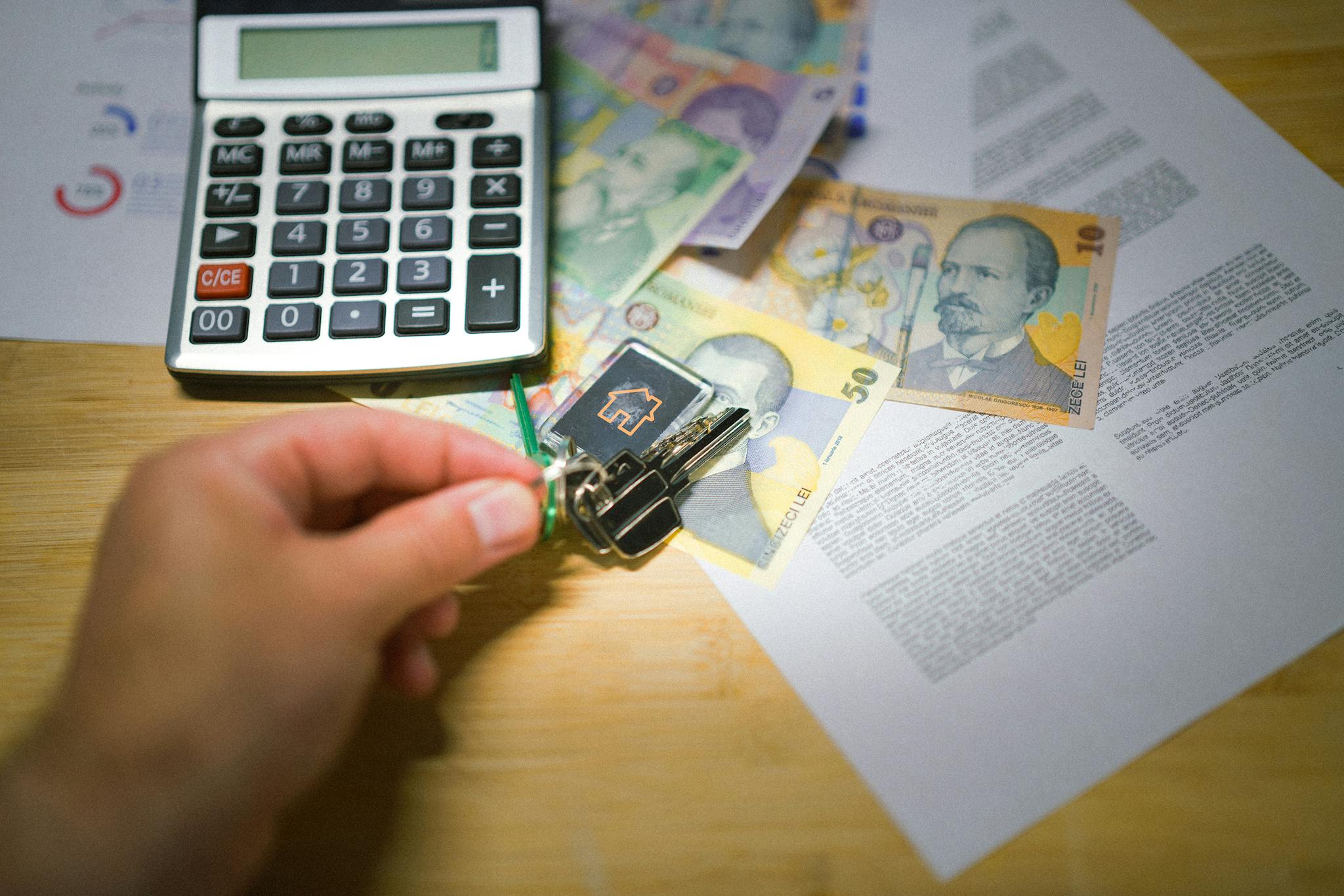 A hand holds keys next to Romanian currency, a calculator, and documents, symbolizing real estate transactions.